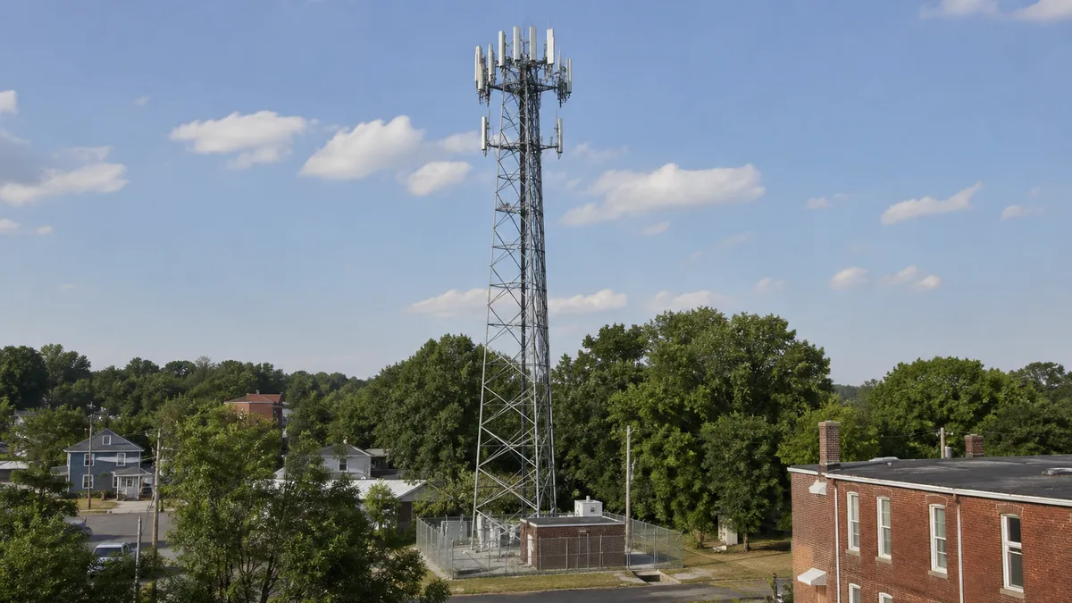 AI-generated scene of a lattice cell tower beside trees and brick buildings.